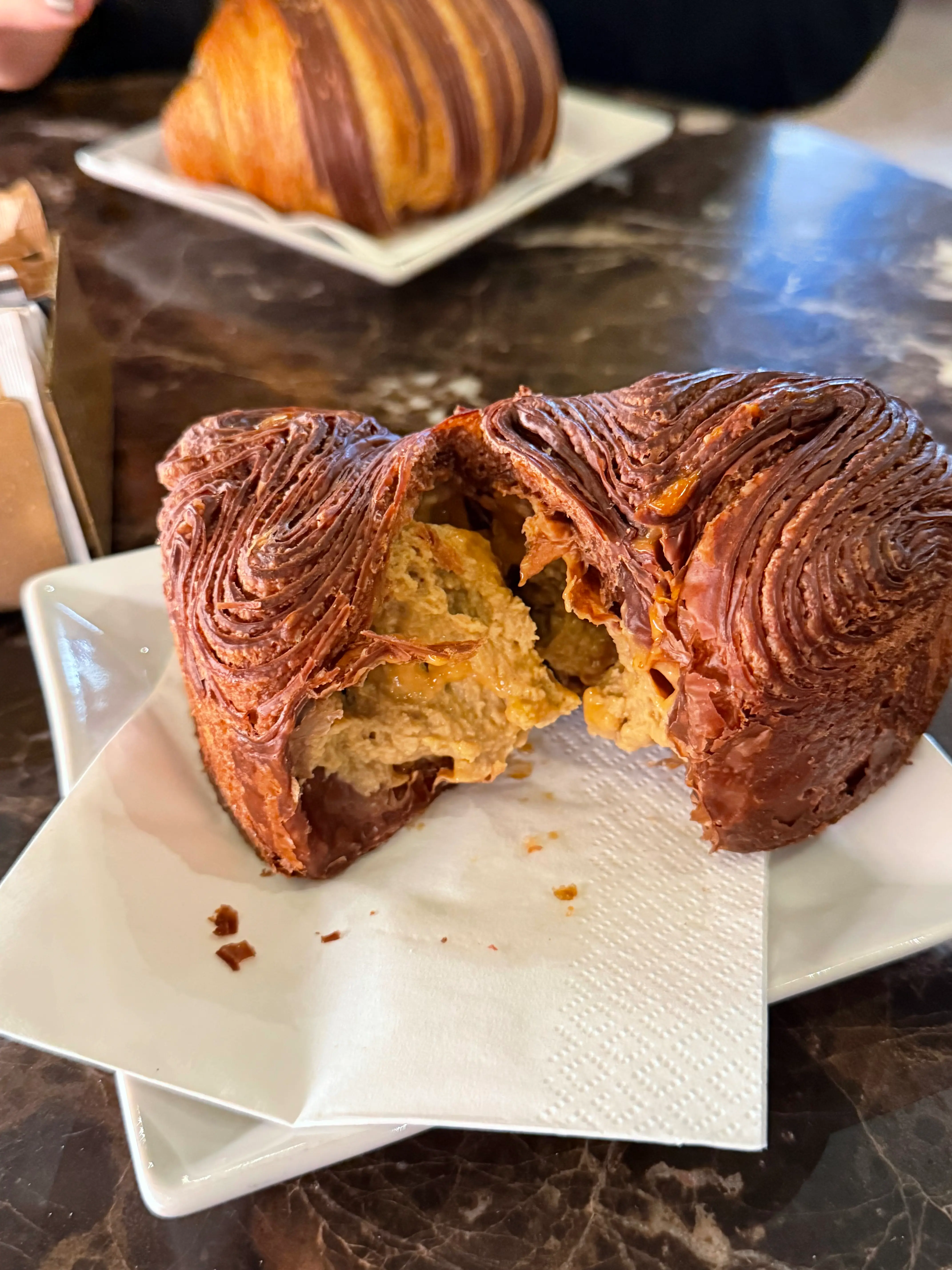 Brioche 'La Carla' del Caffè San Carlo di Torino, aperta a metà su un piattino bianco per mostrare la ricca farcitura interna di crema e la sfogliatura dorata e croccante.
