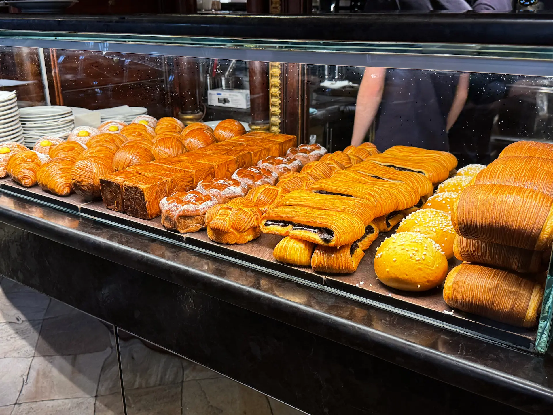 Una vetrina in vetro contenente diverse varietà di brioche e dolci di sfoglia ordinati in file sul bancone della Farmacia del Cambio a Torino.